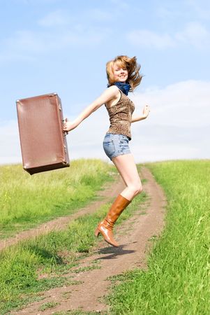 attractive young blond woman with an old leathern suitcase jumping outdoor on the roadの写真素材