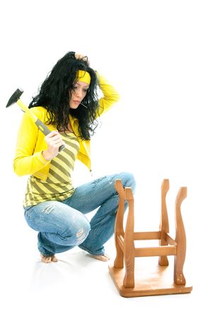 puzzled young brunette woman with a hammer repairs an old chairの写真素材