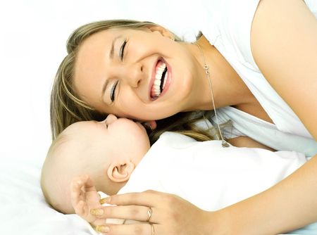 happy young beautiful mother lies on the sofa with her baby and laughsの写真素材