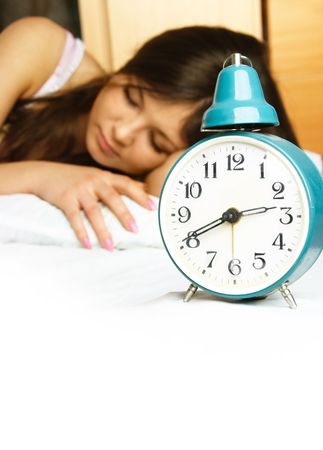beautiful young woman sleeping peacefully in her bed with the alarm clock standing near herの写真素材