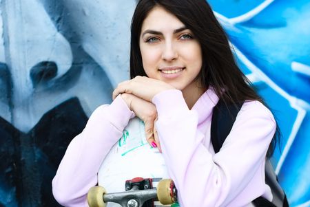 pretty teenage girl with a skate board sitting by the wall with graffiti outdoor