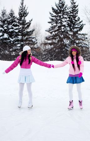 two beautiful girls wearing warm winter clothes ice skatingの写真素材
