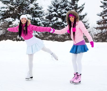 two beautiful girls wearing warm winter clothes ice skatingの写真素材