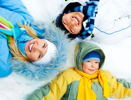 young parents and their son wearing warm winter clothes lie on the snowの写真素材