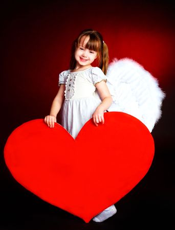 cute little girl with angel wings and a big heart in her handsの写真素材