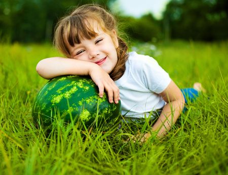 cute little girl with a water-melon on the grass in summertimeの写真素材