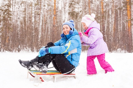 happy family; young mother and her daughter with a sled having fun in the winter park (focus on the child)の写真素材