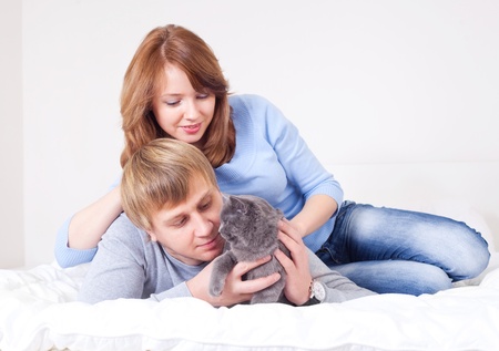 happy young couple on the bed at home with their cat (focus on the man)の写真素材