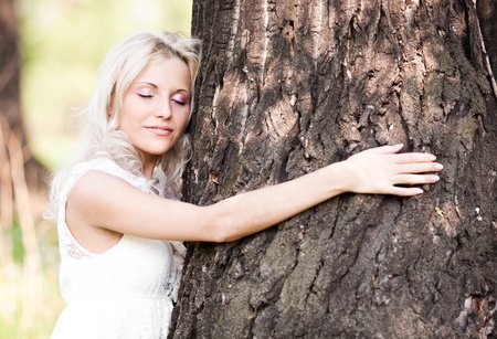 beautiful young blond woman embracing a big tree  on a warm summer dayの写真素材