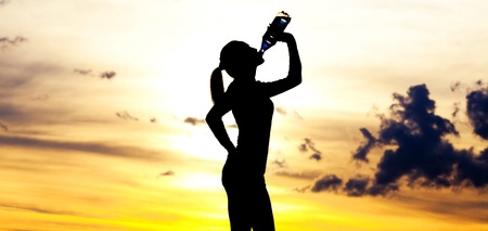 Silhouette of a  woman drinking water on the hill against yellow sky with clouds の写真素材