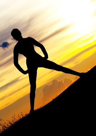 Silhouette of a young woman on the hill against yellow sky with cloudsの写真素材