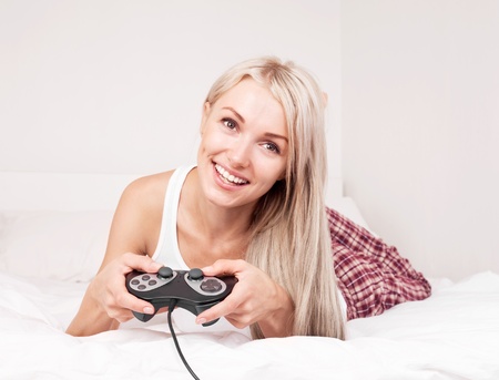 beautiful young blond woman playing computer games on the bed at homeの写真素材