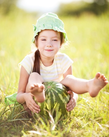 cute little girl with watermelon on the grass in summertimeの写真素材