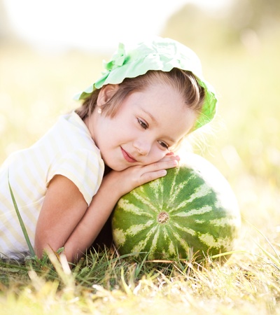 cute little girl with watermelon on the grass in summertimeの写真素材