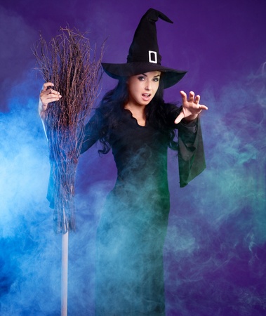 angry sexy young brunette witch with a broom and foam around her, isolated against white backgroundの写真素材