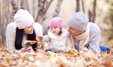 happy young family with their daughter spending time outdoor in the autumn park (focus on the woman)の写真素材