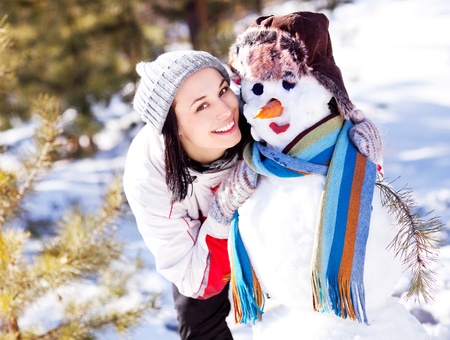 portrait of a pretty young brunette woman with a snowman outdoor on a warm winter dayの写真素材