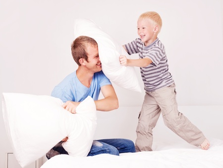 happy laughing father and  son having a pillow fight in bed at home (focus on the man)の写真素材