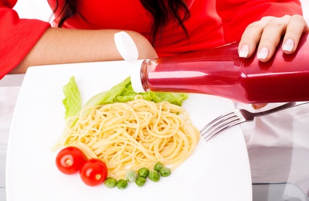 hands of a woman eating spaghetti with tomatoes, salad and peas and adding ketchupの写真素材