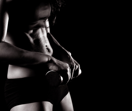 black and white picture of the waist and hands of a beautiful sporty muscular woman working out with two dumbbells, isolated against black background (focus on the belly) の写真素材