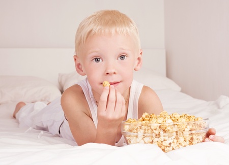six year old boy boy eating popcorn in bed at homeの写真素材