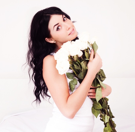 beautiful young brunette woman with roses in bed at homeの写真素材