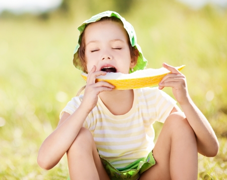 cute happy  little girl with melon on the grass in summertimeの写真素材