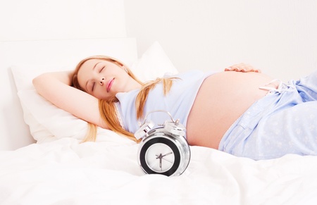 beautiful young pregnant woman with alarm clock in bed at home 