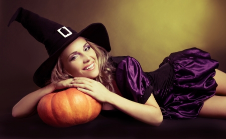 happy young  witch with  a pumpkin,  against yellow studio backgroundの写真素材
