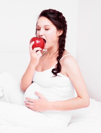 beautiful young pregnant woman eating an apple in bed at home  の写真素材