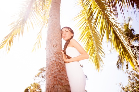 beautiful young woman standing near the palm treeの写真素材