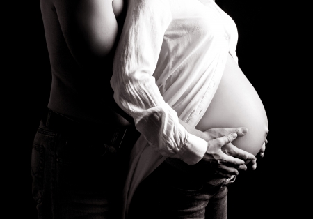 black and white picture of the hands and torso of a pregnant woman and her husband, isolated on black studio backgroundの写真素材