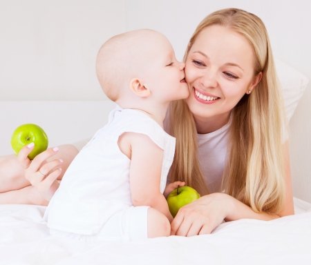 young mother and baby eating apples in bed at homeの写真素材