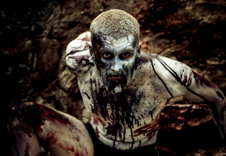 young man with a zombie body painting, covered with blood on the beach against a cliffの写真素材
