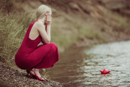 lonely young blond woman with a paper boat by the lake in summertimeの写真素材