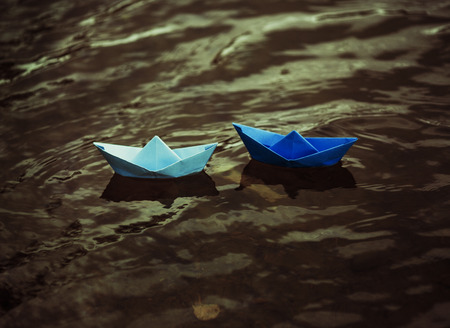 two blue paper boats on the dark water of the lakeの写真素材
