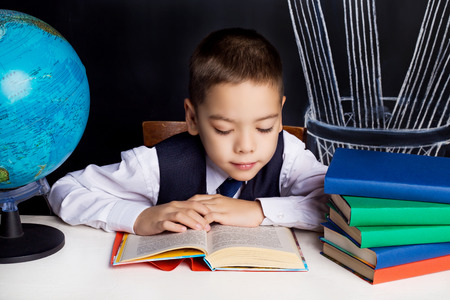 seven year old school boy sitting by the table and reading a bookの写真素材