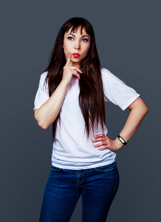 thoughtful young brunette woman against grey studio backgroundの写真素材
