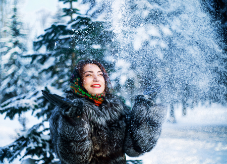 happy woman thrwing snow above her head in the winter park, focus on the flying snowの写真素材