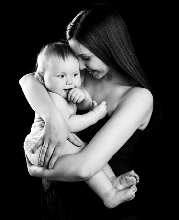 black and white portrait of a happy mother holding her baby, isolated against black studio backgroundの写真素材