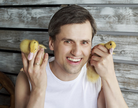 young handsome farmer with two ducklings against wooden wallの写真素材