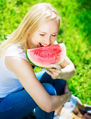 beautiful blond woman eating watermelon in the summer parkの写真素材