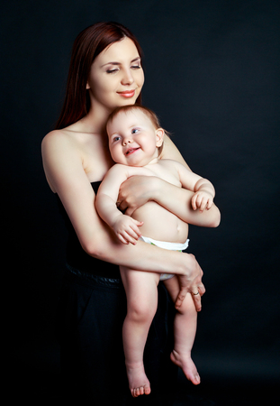 studio portrait of a happy mother holding her baby, isolated against black studio backgroundの写真素材