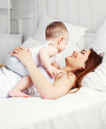 happy beautiful mother with her one year old son in bed at homeの写真素材