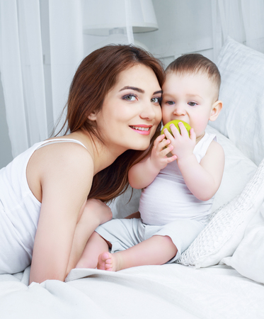 happy beautiful mother with her one year old son in bed at homeの写真素材