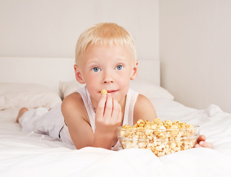 happy child watching TV and eating pop corn   in bed at homeの写真素材