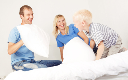 father, mother and son having a pillow fight in bedの写真素材