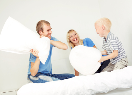 father, mother and son having a pillow fight in bedの写真素材