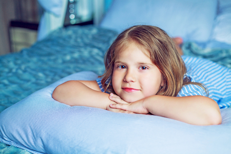 happy little girl with a pillow in bed at homeの写真素材