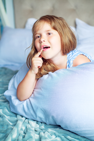 happy little girl with a pillow in bed at homeの写真素材